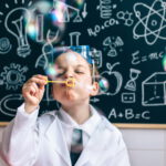 Chłopczyk dmuchający bańki mydlane przed tablicą szkolną