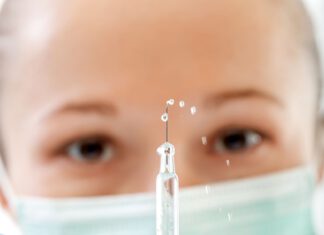 kobieta w masce trzyma w ręku mała strzykawkę używaną do szczepień