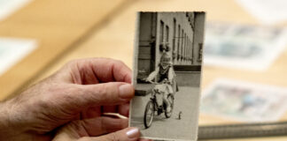 Dwie dłonie, kobieca i męska trzymają stare, czarno-białe zdjęcie. Na zdjęciu dziewczynka na w stroju ludowym na rowerku.