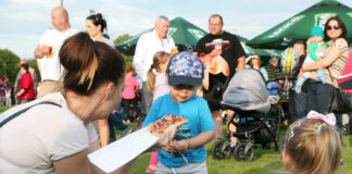 Impreza plenerowa, młoda kobieta częstuje dziecko zapiekanką