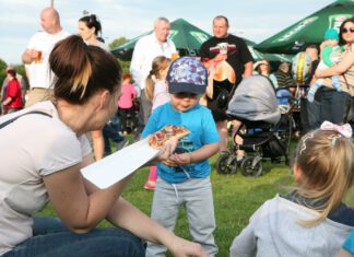Impreza plenerowa, młoda kobieta częstuje dziecko zapiekanką