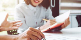 kobieta siedzi przy biurku z notatnikiem i długopisem w ręku.