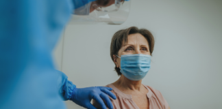 obrazek poglądowy, starsza osoba - kobieta w maseczce w trakcie szczepienia w ramię