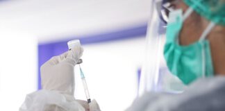 zdjęcie poglądowe - pracownik medyczny w fartuchu i masce przygotowuje strzykawkę ze szczepionką