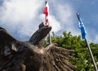 Widok orła - części Grobu Nieznanego Żołnierza na Skwerze Kombatantów w Kwidzynie, na tle flagi polskiej i Kwidzyna