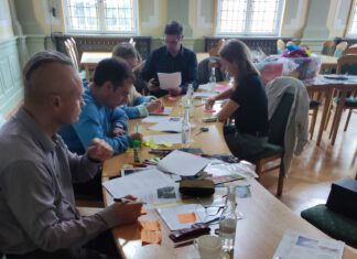 uczestnicy warsztatów siedzą przy stole, wycinają i piszą