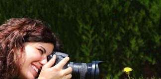 kobieta leży na trawie z apaaratem i fotografuje mlecz