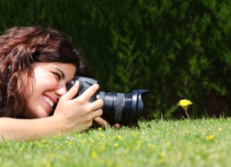 kobieta leży na trawie z apaaratem i fotografuje mlecz
