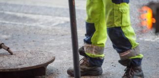 otwarta studzienka kanalizacyjna, nad nią stoi robotnik