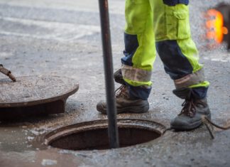 otwarta studzienka kanalizacyjna, nad nią stoi robotnik