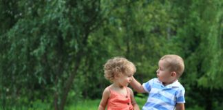 dwoje małych dzieci siedzi na przewróconym drzewie