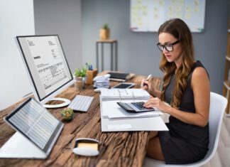 Księgowa przy biurku przed ekranem liczy na kalkulatorze