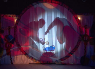 dekoracja teatralna - koło, w środku łóżeczko, na które dwie postaci odkładają dziecko