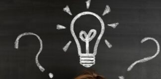 kobieta myśląca - w tle tablica z narysowaną kredą żarówką i znakami zapytania