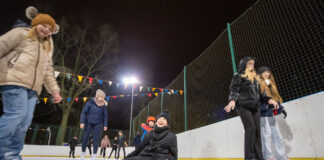 Zabawa dzieci i młodzieży na lodowisku. Rozśmiana dziewczyna w centrum